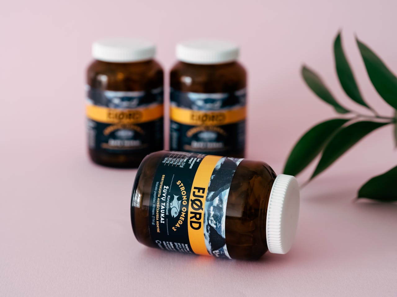 Amber vitamin bottles with a leafy accent on a pink surface, evoking wellness.